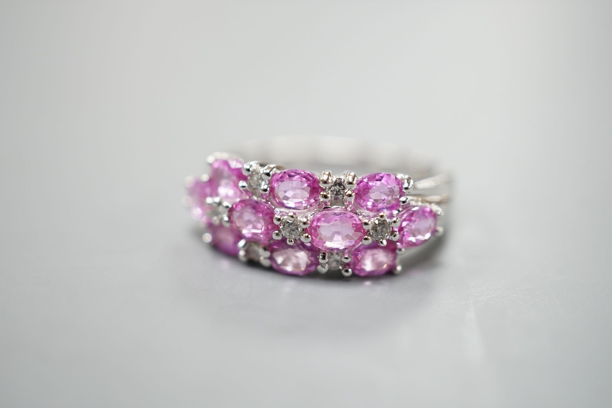 A modern 14k white metal, pink sapphire and diamond cluster set half hoop dress ring, size O, gross weight 4.6 grams.